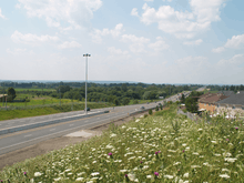 A freeway changes into a four-lane conventional road, and vanishes into the rural foothills