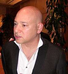 A bald man wearing a white shirt and a black jacket.