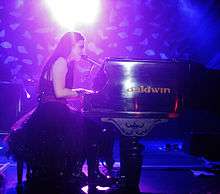 Young woman with long, dark hair singing and playing piano onstage