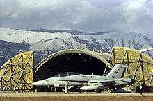 An F/A-18D on the parking ramp in front of an armored hangar in Aviano Air Base