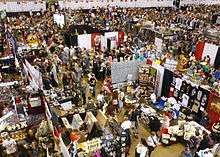 Photograph of the Expo in progress, taken from a high vantage point, showing crowds of attendees among booths arranged in a grid.