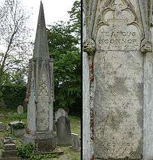 A granite funerary monument in the shape of a spire among other headstones