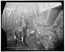 Two dirty men feeding coal into an oven in a rather gloomy looking room