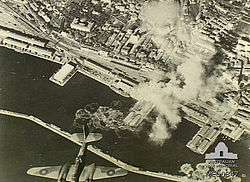 Aerial view of port and plumes of smoke caused by explosions with a bomber in the foreground