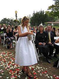 Smiling girl scattering flower petals at an outdoor wedding