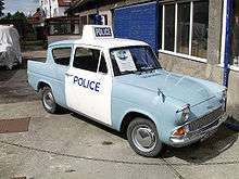Ford Anglia car in pale blue paint, with white overpainted doors and roof. The roof also carries a Police lightbox sign and flashing blue light.