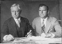 Photograph taken circa 1930 of Burnham with his son Roderick.  Frederick Burnham is on the left, and Roderick Burnham is on the right.  Both men are wearing suits and ties and they seated at a table with many papers in front of them.