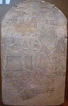 A stone stela with raised-relief images of a man seated with his son and wife, while a man stands to the right giving libations; Egyptian hieroglyphs are written in distinctly-marked horizontal columns at the bottom portion of the stela.