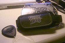 The "Guitar Grip", a hand-sized unit that fits into the Nintendo DS with four colored fret buttons on one end, and an adjustable strap that the player wears to hold the Grip and DS in place while playing. The Grip features the "Guitar Hero: On Tour" logo on one side.