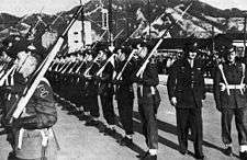 Soldiers in formal uniform with slouch hats, blancoed web belts, garters and slings being inspected on parade