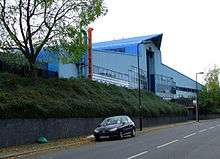 A large, blue, triangular building at the top of a plant covered embankment.