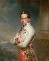 Half-length oil portrait of the Archduke Charles. He wears a white high-collared military jacket of the Austrian army and has a red and white sash over his right shoulder. He wears two decorations, a cross on his breast and another medal at his neck. Charles has a long fleshy face, short brown hair and light eyes. He gazes calmly towards the viewer. His arms are folded across his chest.