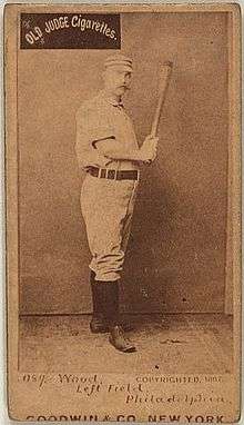 A sepia-toned baseball card image of a man wearing an old-style white baseball uniform and cap and holding a baseball bat