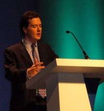 Osborne speaking at a podium, gesturing with his hands.