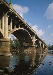 A photograph from a low angle of a arch bridge spanning a river.