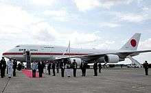 Parked VIP aircraft with red carpet and assembled entourage.