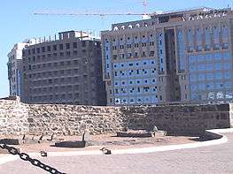Low stone wall with remains of sarcophagi next to modern buildings