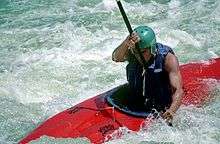 Man wearing helmet sitting in fiberglass boat, paddling through frothy water