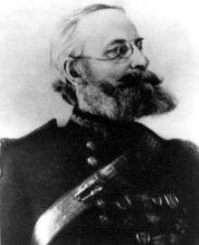 Profile of an older white man with a full, bushy beard and wire-framed glasses wearing a military jacket with shoulder boards, many medals on the left breast, and a strap running diagonally across the chest.