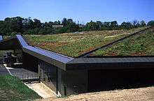  A low building has a roof completely covered with soil and grass. It appears to be built into a hillside