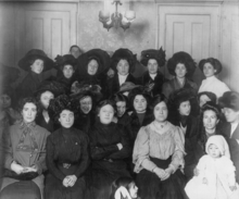 A large group of women wearing dark, early 20th century clothing pose for the camera.