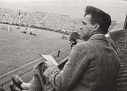 Journalist, seated in the stands and speaking into a microphone