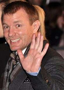 Guy Ritchie smiling and waving his hand