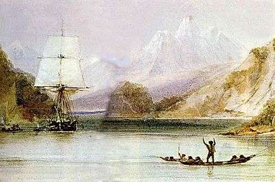 On a sea inlet surrounded by steep hills, with high snow-covered mountains in the distance, someone standing in an open canoe waves at a square-rigged sailing ship, seen from the front