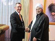 Two men, one in a suit and the other in Islamic dress, shaking hands