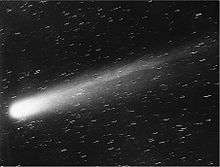 Black-and-white picture of the comet, its nucleus brilliant white, and its tail very prominent, moving up and to the right