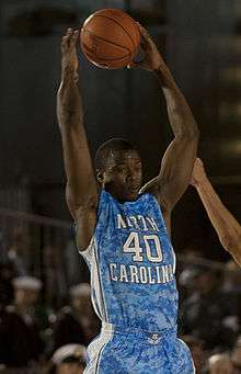 A basketball player wearing a light blue camouflage jersey holding the ball in the air.