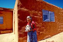 Helen Cordero standing by an adobe building in 1986