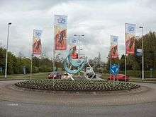 A roundabout with a sculpture in the middle of it, and banners depicting cyclists hanging around it