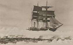  Three masted ship with sails spread, surrounded by pack ice, with a narrow lane of water in the foreground