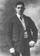 A black and white photograph showing an early middle-aged man with short, uncovered Afro-textured hair posing in a suit.