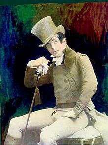 A young man dressed all in white with a matching top hat and cane sits, head cocked, looking to his left