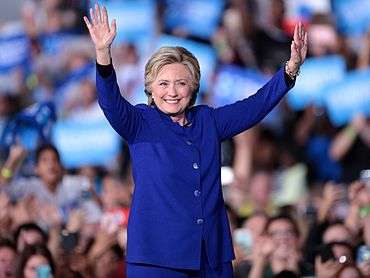 Clinton in a blue suit, looking toward the camera. Audience members in the background. She is at a speaking event in Tempe on November 2, 2016.