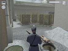 A man wielding gun looks across the unconscious, naked body of a guard in an outside storage facility.