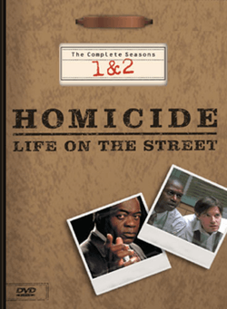 A DVD box-set cover with a background resembling a brown file folder, including a metal clip at the top. The words "Homicide: Life on the Street" are printed in the middle of the cover, with the words "The Complete Seasons 1 & 2" above it. Underneath the words are two images resembling photographs, one with a man wearing a suit jacket looking straight forward and pointing with his index finger, and the other of two men wearing dress shirts leaning forward and looking sideways.