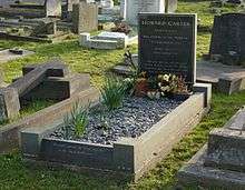 A polished, black granite headstone with freshly planted flowers, among other gravestones