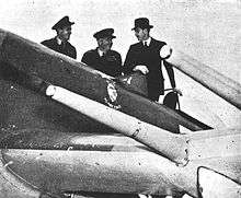 Three men stand next to a fighter aircraft and look at it