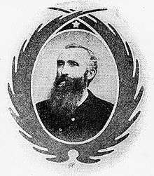 Framed portrait of a white man with a very long beard, neatly trimmed hair, and a dark jacket.