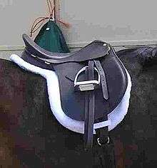 An English saddle set on top of a white pad that has the same shape as the saddle