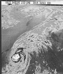 Grayscale image of a well-organized tropical cyclone near the lower-left corner of the image. Although most of the clouds are concentrated towards the lower-left, clouds from the storm extend to the upper-right corner.