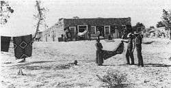 Photo of Navajo woman and two white men holding a blanket in front of a building