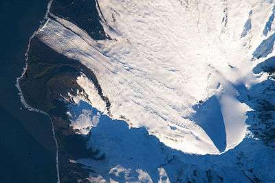 Satellite image of a snow-covered volcanic peak, with a glacier running straight into the ocean