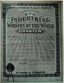 Framed, formal document featuring various IWW themes, cursive body text, hand-filled forms and a stamped seal.
