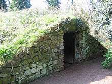A mound-shaped structure covered in grass. At the front is a stone wall with a doorway.