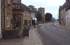 Street scene showing a pub the Ilchester Arms on the left with several other buildings leading to a church tower.