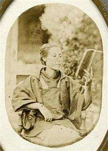 Monochrome photograph of an elderly Kusumoto Ine seated and reading a book